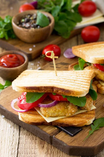 Club sandwich with tomatoes, cheese, crispy chicken nuggets and arugula. Delicious fresh homemade club sandwich with chicken on a wooden kitchen table. Street food, fast food. Copy space.
