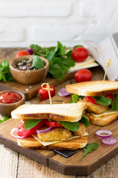 Club sandwich with tomatoes, cheese, crispy chicken nuggets and arugula. Delicious fresh homemade club sandwich with chicken on a wooden kitchen table. Street food, fast food. Copy space.