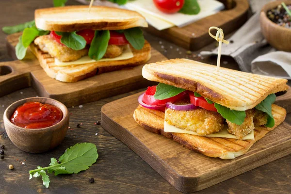 Sandwich with Tomatoes, Cheese, Crispy Chicken Nuggets and Arugula.  Delicious fresh homemade club sandwich with chicken on a wooden table. Fast food