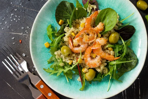 Diet menu, Vegan food. Healthy salad close-up with quinoa, arugula, Shrimps and olives on a dark stone table.