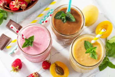 Çilek, çikolata ve kayısı milkshake veya smoothies Beyaz ahşap zemin üzerinde. Sağlıklı sulu vitamini içki diyet veya vegan gıda kavramı. 