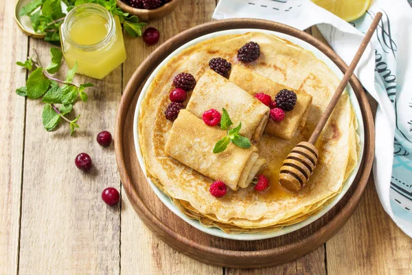 Healthy Pancakes breakfast. Stack of homemade thin pancakes or crepes on a rustic table, served with honey and fresh berries. Copy space