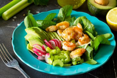 Izgara karides, rucola, turp, avokado, kereviz ve salata sosu karanlık arduvaz arka plan üzerinde sağlıklı sebze salatası. Diyet menüsü. 