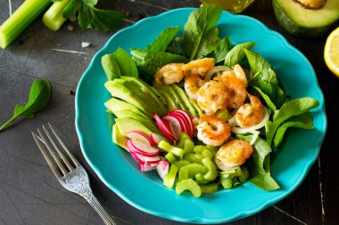 Izgara karides, rucola, turp, avokado, kereviz ve salata sosu karanlık arduvaz arka plan üzerinde sağlıklı sebze salatası. Diyet menüsü. 