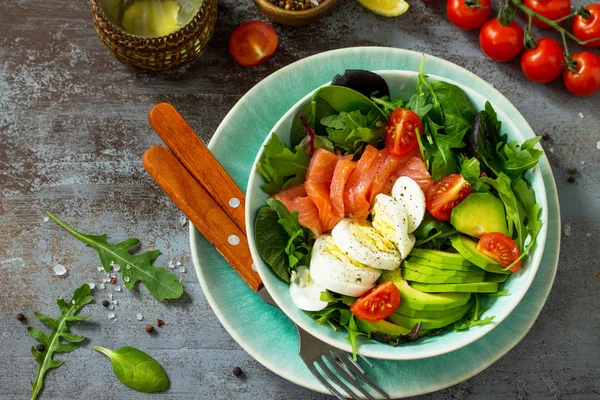 Diet menu concept. Summer Healthy salad with Tomatoes, Salmon, Egg, Avocado and arugula on a dark stone table. Top view flat lay background.