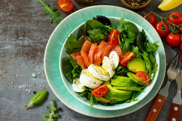Diet menu concept. Summer Healthy salad with Tomatoes, Salmon, Egg, Avocado and arugula on a dark stone table.