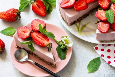 Yaz diyeti tatlısı, peynirli kek, pişirmeden. Çikolatalı granola üzerine çilekli kek ve açık gri bir masada taze çilek..