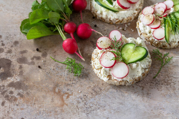 Crispbread sandwiches with ricotta, radish and fresh cucumber on a light kitchen stone or slate countertop. Copy space