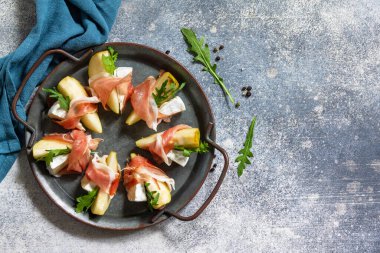 Yaz atıştırmalıkları. Jamonlu armut aperatifi, roka ve brie peyniri. Üst görünüm düz arkaplan. Boşluğu kopyala