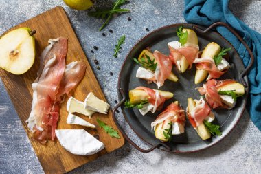 Yaz atıştırmalıkları. Jamonlu armut aperatifi, roka ve brie peyniri. Üst görünüm düz arkaplan. 
