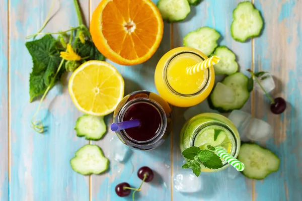 夏の様々な軽食ドリンク チェリージュース デトックスキュウリの水と青い木製のテーブルの上のオレンジジュース トップ表示フラットレイアウトの背景 — ストック写真