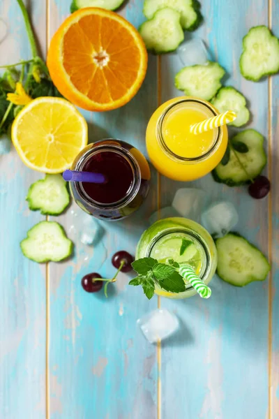 夏の様々な軽食ドリンク チェリージュース デトックスキュウリの水と青い木製のテーブルの上のオレンジジュース トップビューのフラットレイアウトの背景 スペースのコピー — ストック写真
