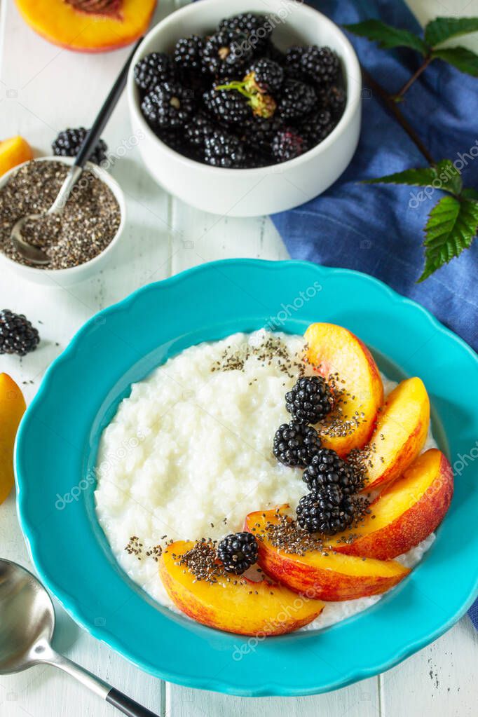Healthy food for Breakfast, diet food concept. Rice porridge with chia, peach and blackberry in a bowl on a white wooden table.