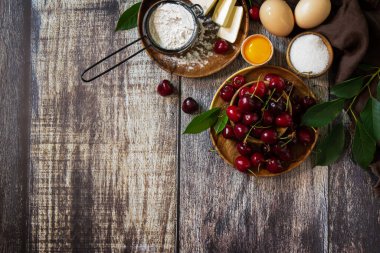 Kiraz pişirme mevsimi konsepti. Kırsal bir ahşap masada kirazlı turta (kırmızı kiraz, un, yumurta, şeker ve tereyağı) için malzemeler. Düz bir yatağın üst görüntüsü. Boşluğu kopyala.