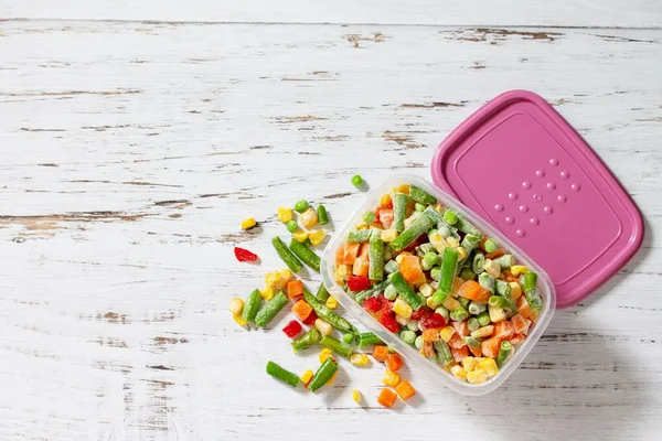 Healthy food is frozen. Containers frozen vegetable mixture of pepper, carrots, corn and peas. Top view flat lay background. Copy space.