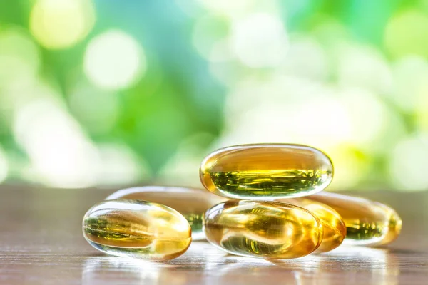 fish oil supplement capsules in selective focus on top wooden table with green natural bokeh background
