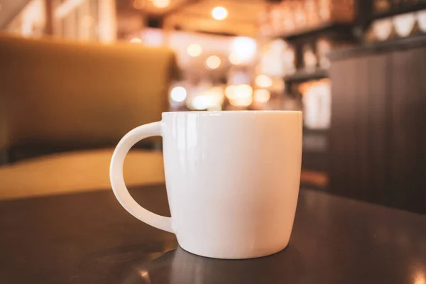 A cup of hot coffee on top of wooden table in coffee shop with warming vintage color tone, coffee shop background