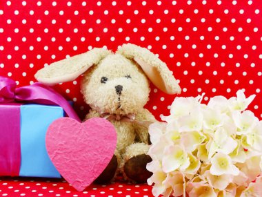 tavşan bebek pembe kalp hediye kutusu ve kırmızı puantiyeli arka plan üzerinde yapay çiçek