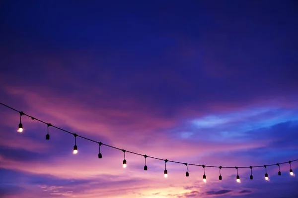 light bulbs on string wire against sunset sky by the beach