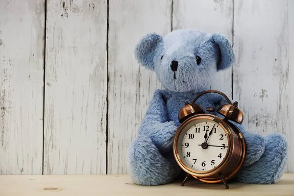 blue teddy bear and alarm clock with space copy on wooden background