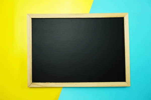 黄色と青の背景のフラットに空の黒板を置く — ストック写真