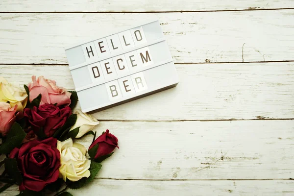 Top View Hello December alphabet letters with light box and flowers bouquet on wooden background
