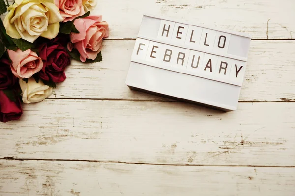 Top View Hello February alphabet letters with light box and flowers bouquet on wooden background