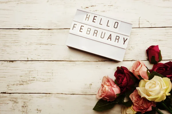 Top View Hello February alphabet letters with light box and flowers bouquet on wooden background