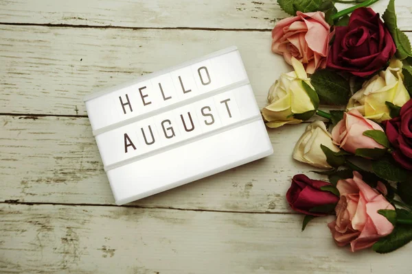 Top View Hello August alphabet letters with light box and flowers bouquet on wooden background