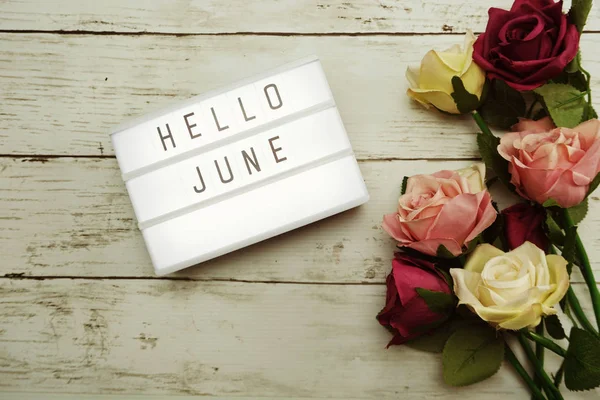 Top View Hello June alphabet letters with light box and flowers bouquet on wooden background