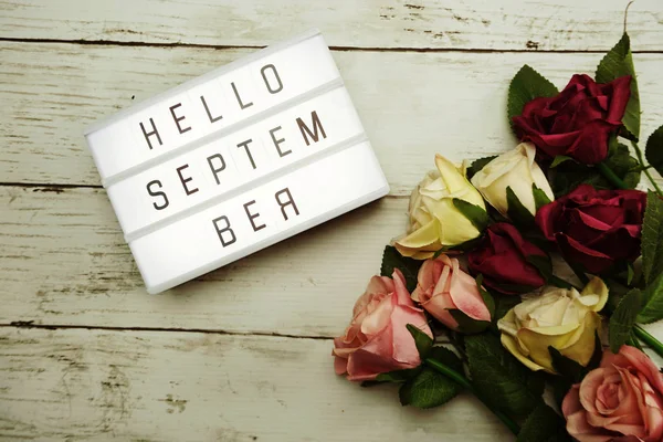 Top View Hello September alphabet letters with light box and flowers bouquet on wooden background