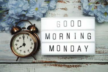 Günaydın pazartesi günü alarm saati ve ahşap arka planda çiçek desenli ışık kutusunda.