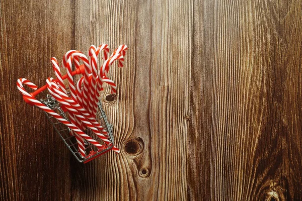 Christmas Candy Cane in mini shopping cart on wooden background