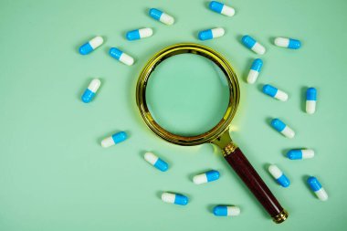 İlaç kapsülü ve yeşil zemin üzerindeki büyüteç