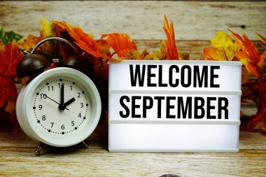 Alarm saati ve ahşap arka planda akçaağaç yaprağı süslemesiyle Eylül ayına ait metne hoşgeldiniz