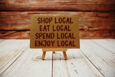 Shop Local, Eat Local, Spend Local, Enjoy Local text message with easel on wooden background