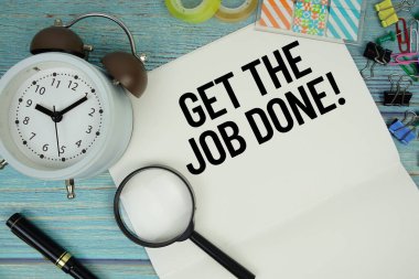 Get The Job Done! text on a paper surrounded by office supplies, a magnifying glass, and a clock on a blue wooden surface