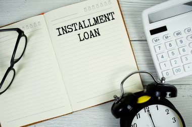 Installment Loan  text on notepad with alarm clock, eyeglasses and calculator on wooden background