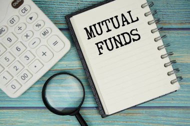 Mutual Funds text on notepad with magnifying glass and calculator on wooden background