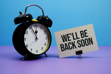 We'll Be Back Soon text with alarm clock on blue and purple background