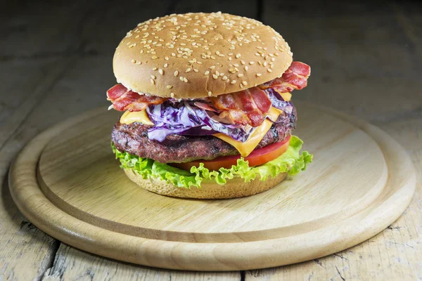 Hamburger with cheese salad tomato bacon and coleslaw on round wooden chopping board