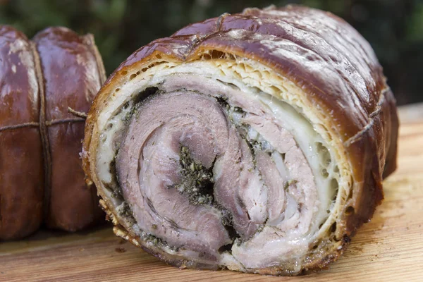 Porchetta roasted rolled pork cut in half on chopping board