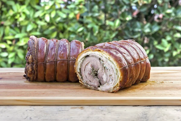 Porchetta roasted rolled pork cut in half on chopping board