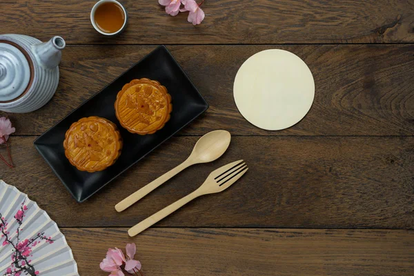 Table top view aerial image of decoration Chinese Moon Festival background concept.Flat lay cake & tea and pink blossom on modern rustic brown wooden wallpaper.Free space for creative design mock up