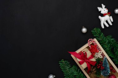 Merry Christmas dekorasyon ve mutlu yeni yıl süsleri kavramı en iyi görünümünü masa. Düz temel nesneleri modern rustik ahşap siyah arka plan üzerine ev stüdyosu ofis masası, Ren geyiği ve hediye kutusu yatıyordu..