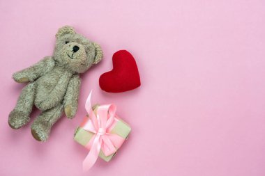 Table top view aerial image of decoration valentine's day background concept.Flat lay essential items love red heart & gift box with bear doll toy kid on modern rustic pink paper with copy space.
