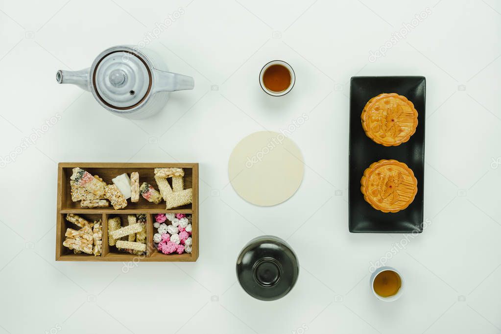 Table top view aerial image Lunar New Year & Chinese New Year concept background.Flat lay essential foot & drink meal set the sweet dessert & cup of tea with moon cake on modern rustic white paper.