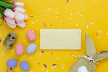Tablo üstten görünüm süslemeleri mutlu Paskalya tatili arka plan kavramı bir kadeh. Düz bunny yumurta ve hediye kutusu konfeti modern rustik sarı kağıt üzerine yatırın. Boş alan Tasarım sahte için yukarı ve şablon.