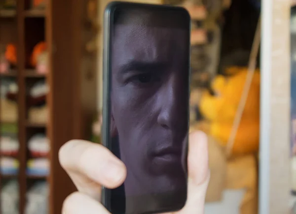 guy looks at the screen of a black smartphone, through the reflection of the screen looks one eye into the camera