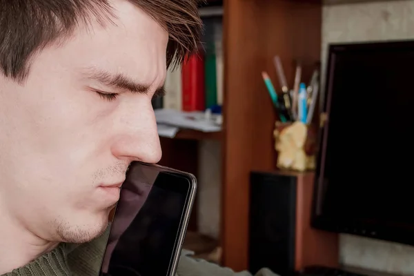 thoughtful guy with a smartphone at his mouth, with his eyes closed, sits at the desk